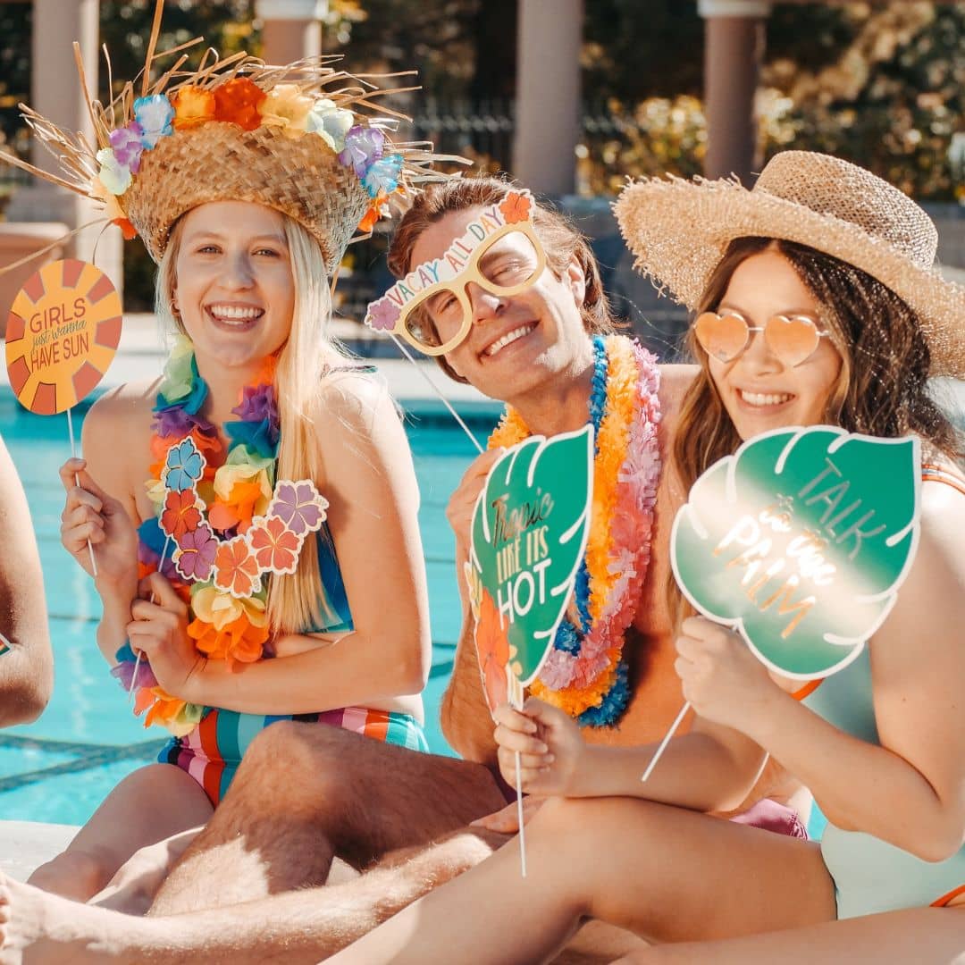 na zdjęciu widać grupę uśmiechniętych ludzi, którzy siedzą przy basenie trzymając hawajskie dekoracje