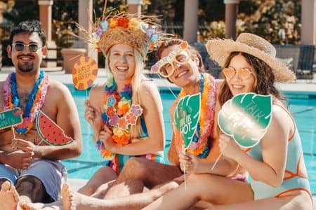 grupa ludzi siedząca nad basenem w strojach kompielowych z hawajskimi dekoracjami