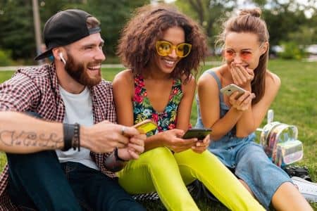 troje uśmiechniętych młodych ludzi pokazuje sobie coś wzajemnie na swoich telefonach